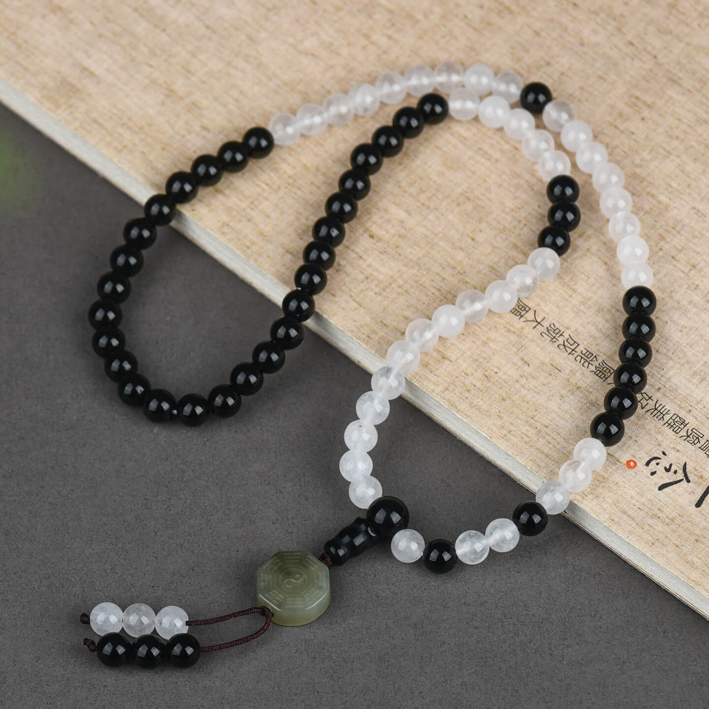 The Hetian Nephrite Flow Pearl bracelet is casually coiled on a dark sandalwood table, showcasing the warm glow of the jade, the contrast of the obsidian, and the refined tactile texture of the beads.