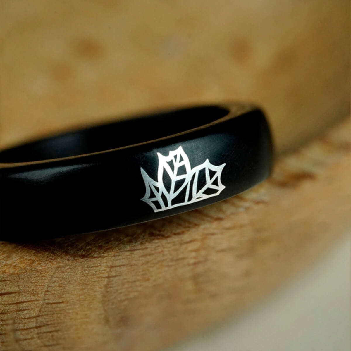 Macro detail of the red sandalwood ring, showcasing the precise silver maple leaf inlay and the wood's natural grain.